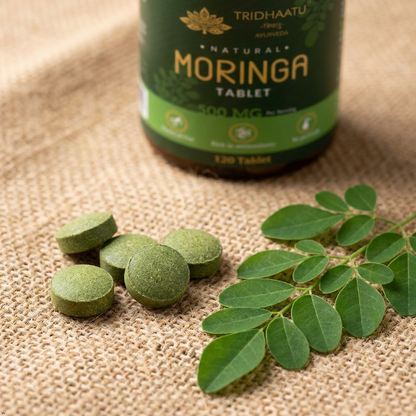 Moringa tablets and leaves with a bottle labeled 'Tridhaatu' on a textured surface